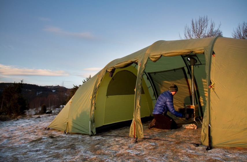 Helsport Lavvu Tält med Kamin, en person håller på med kaminen inuti tältet